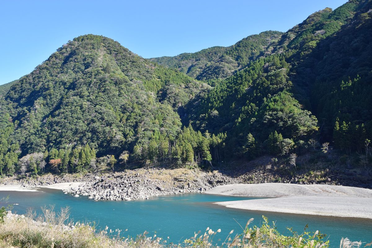 A blue river with white gravel banks between green forested mountains