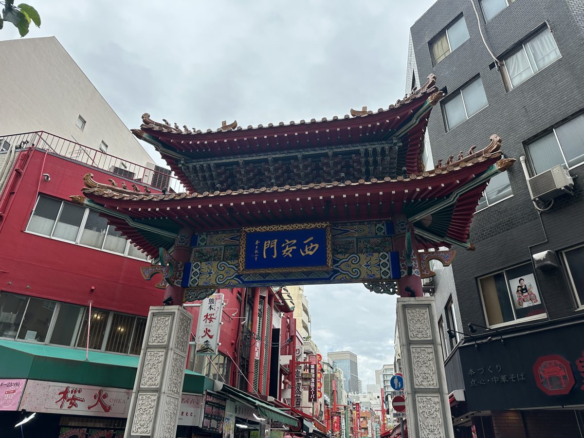 An ornate Chinese gate with green and red roofs over a city street