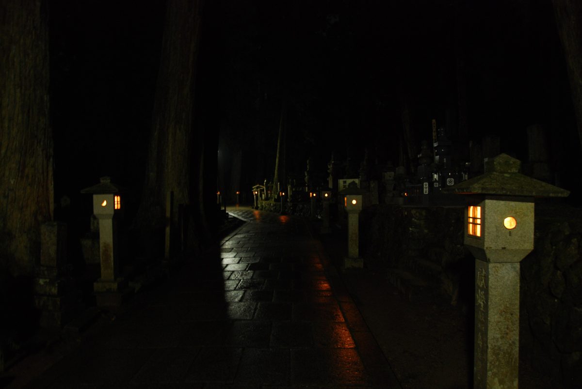 Lit stone lanterns along a dark stone path among cedar trees at Okunoin on Mount Koya at night