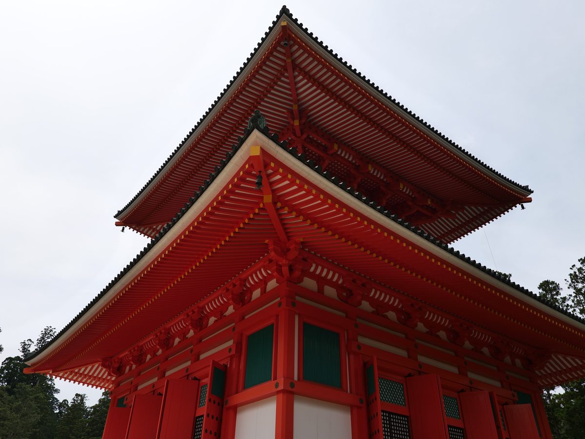 A red pagoda at the Danjo Garan seen from below against a pale sky