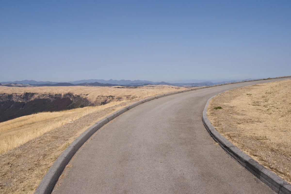 A paved road curving across dry grassland on a mountain ridge under a clear sky