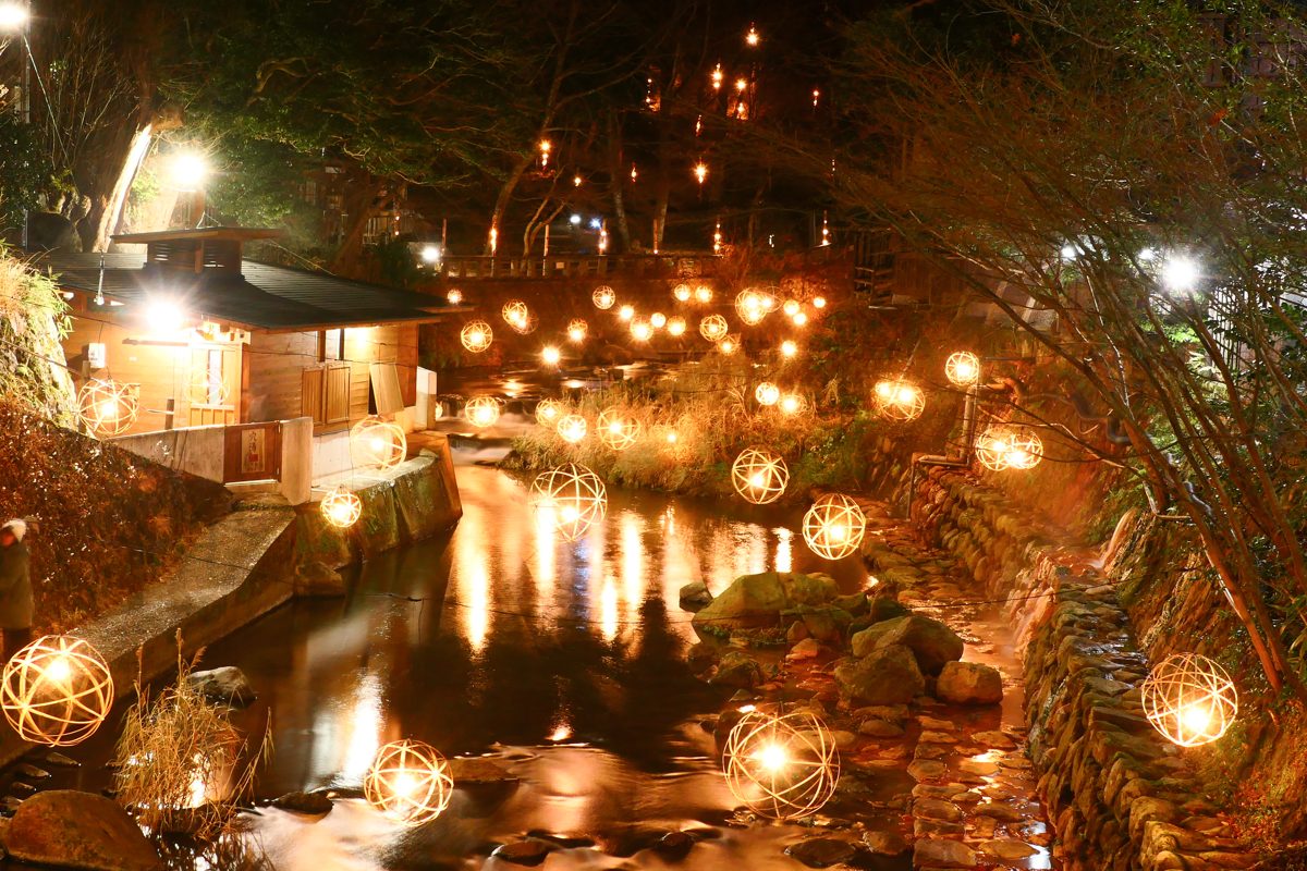 Round lanterns glowing at night along a stream lined with wooden buildings