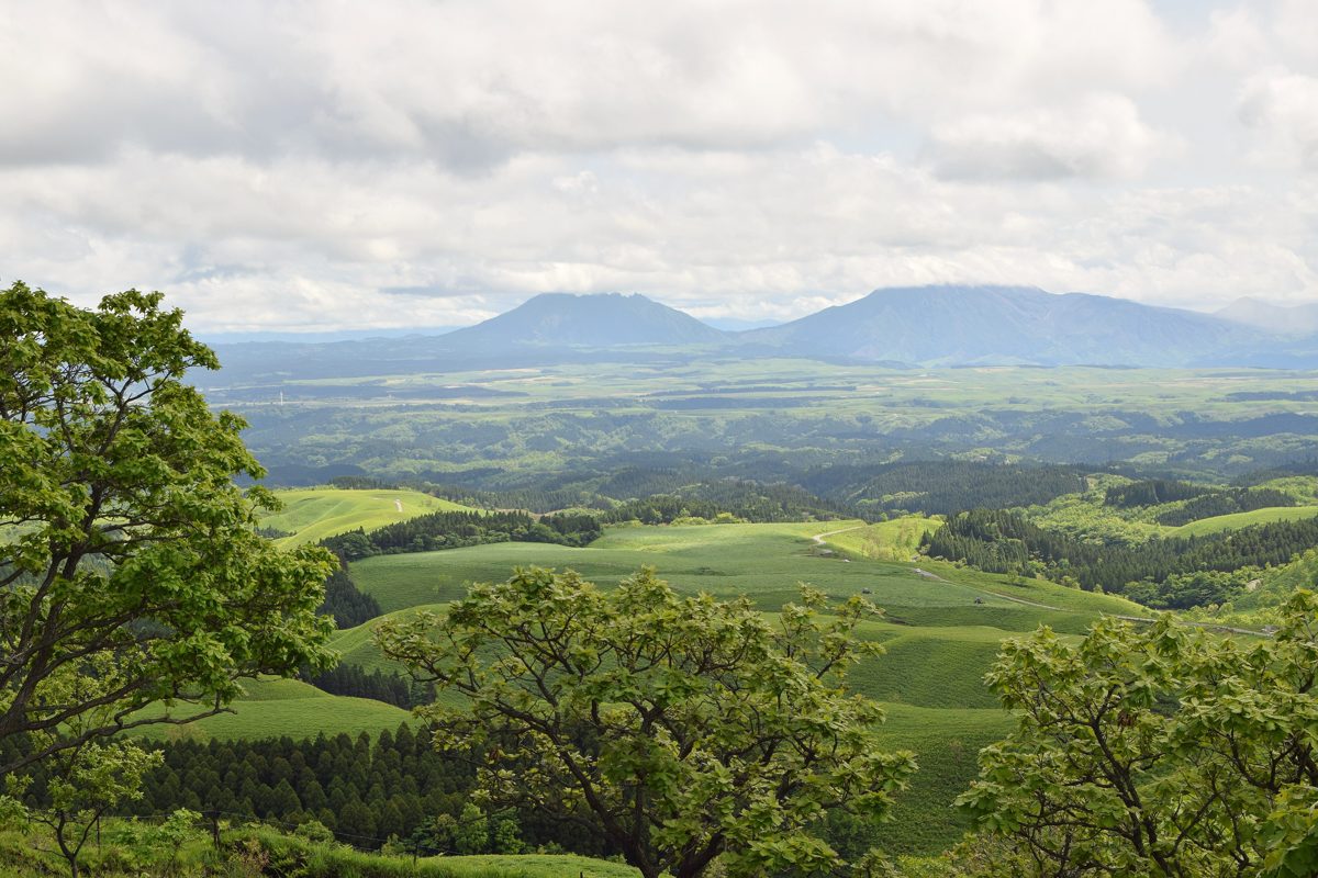 Rolling green hills and farmland under a partly cloudy sky, with mountains on the horizon