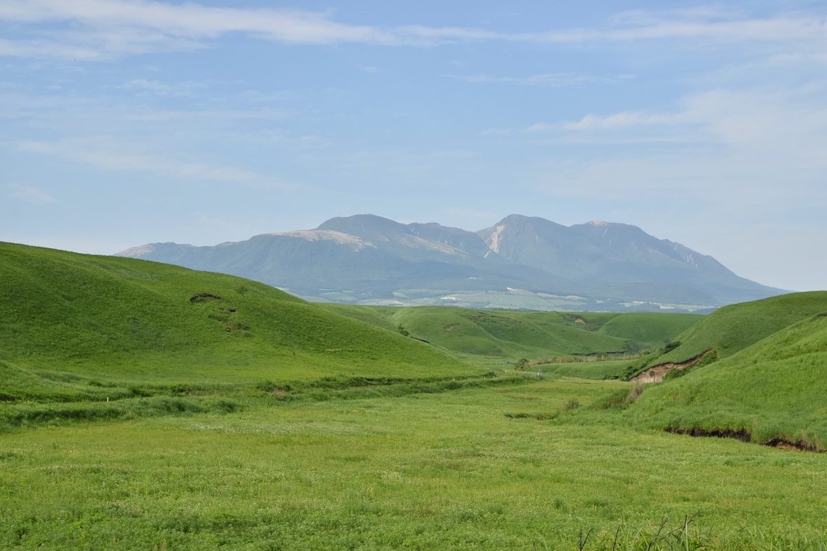 A wide green valley with mountains in the distance under a blue sky