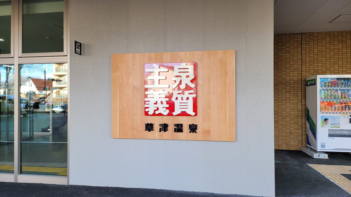 A wooden wall plaque reading Kusatsu Onsen at the entrance of the bus terminal