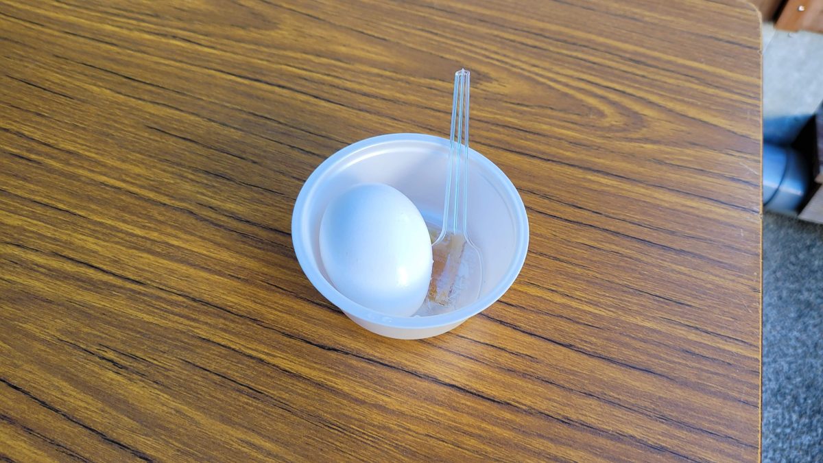 A soft-boiled hot-spring egg in a small plastic cup with a spoon on a wooden table