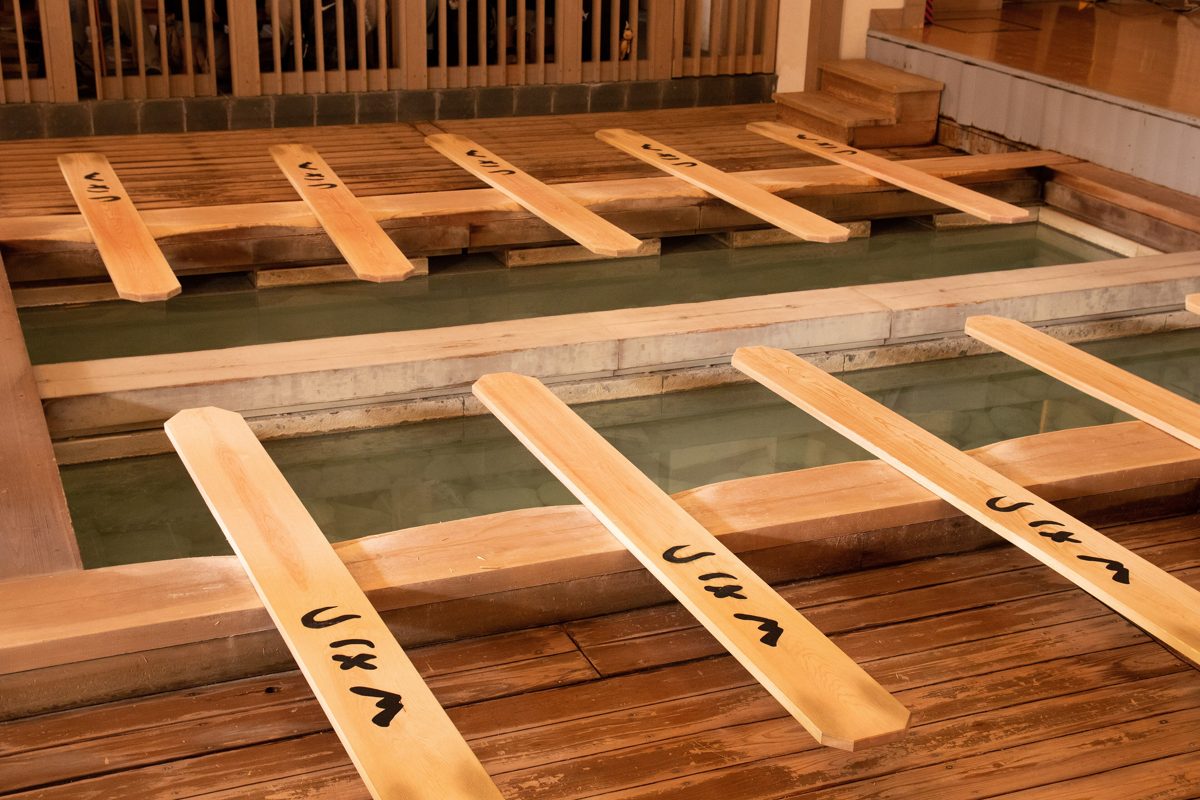 Long wooden paddles resting across a pool of hot-spring water in a wooden hall