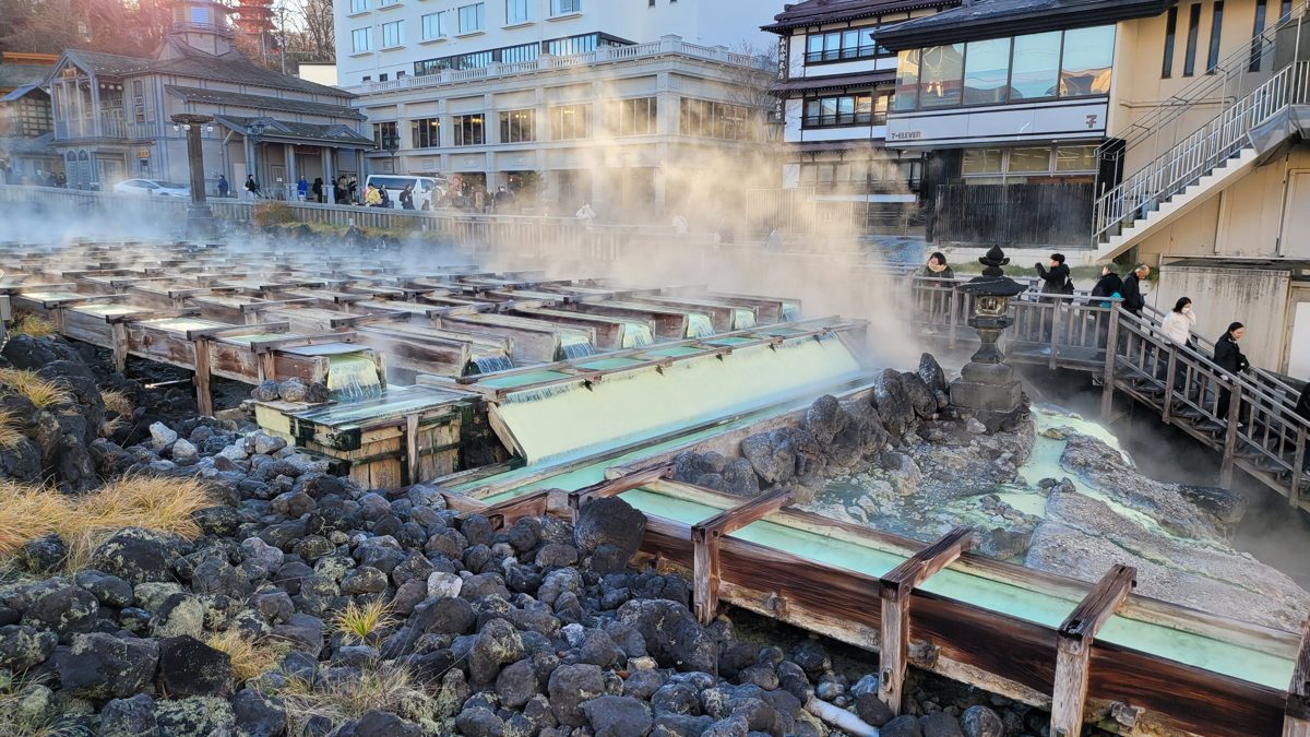 Steam rising from the wooden channels of Yubatake in Kusatsu Onsen on a sunny day