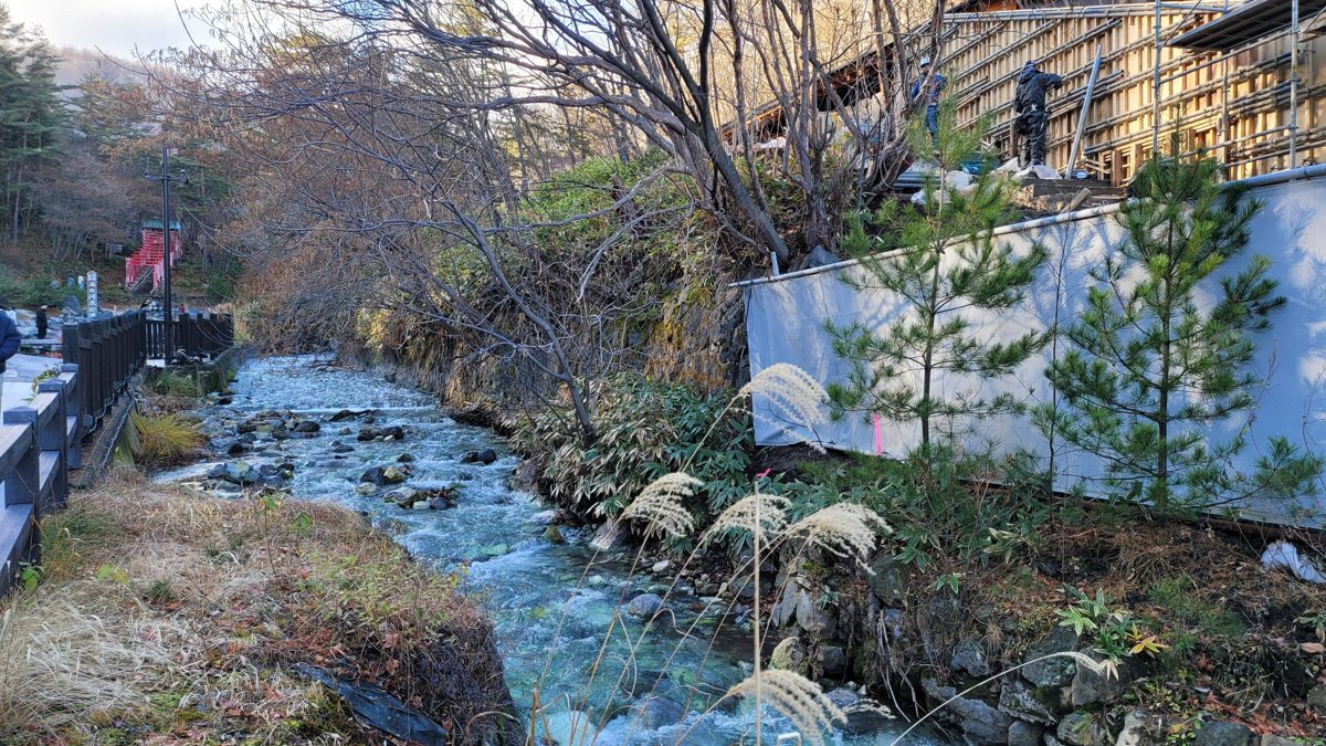 A clear stream running between rocks and dry grass in Sainokawara Park