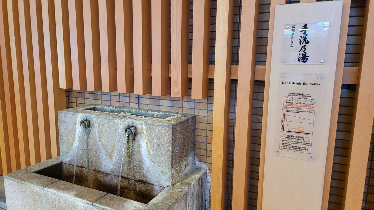 A stone hand-washing basin with two hot-spring spouts and a sign saying not to drink the water