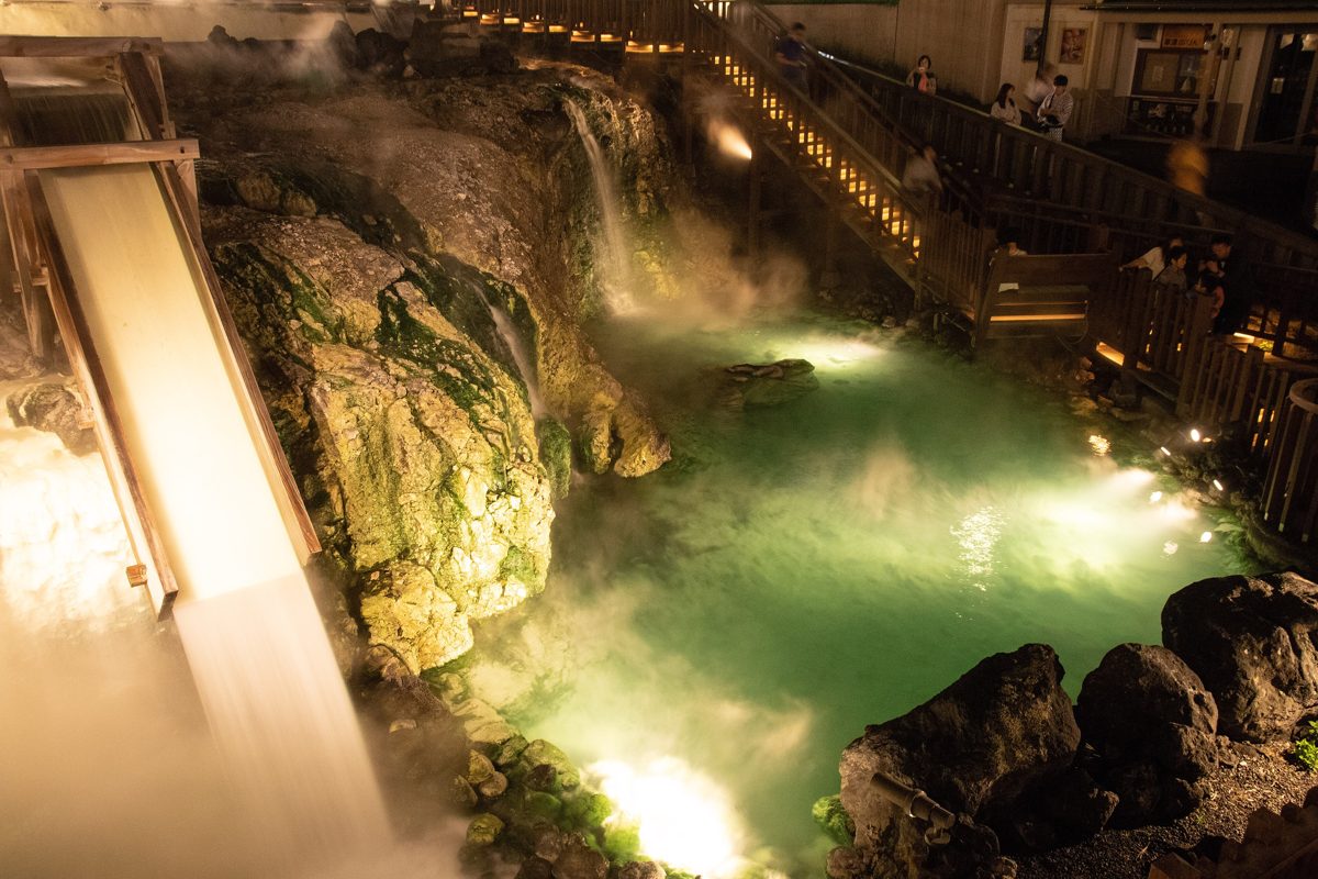 Blue-green hot-spring water flowing over rocks at the Yubatake, lit at night