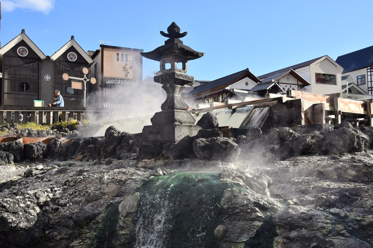 A stone lantern and steaming hot-spring water at the Yubatake in Kusatsu Onsen on a sunny day