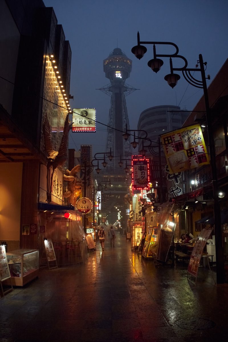 Tsutenkaku Tower at dusk at the end of a narrow street of restaurants in Shinsekai
