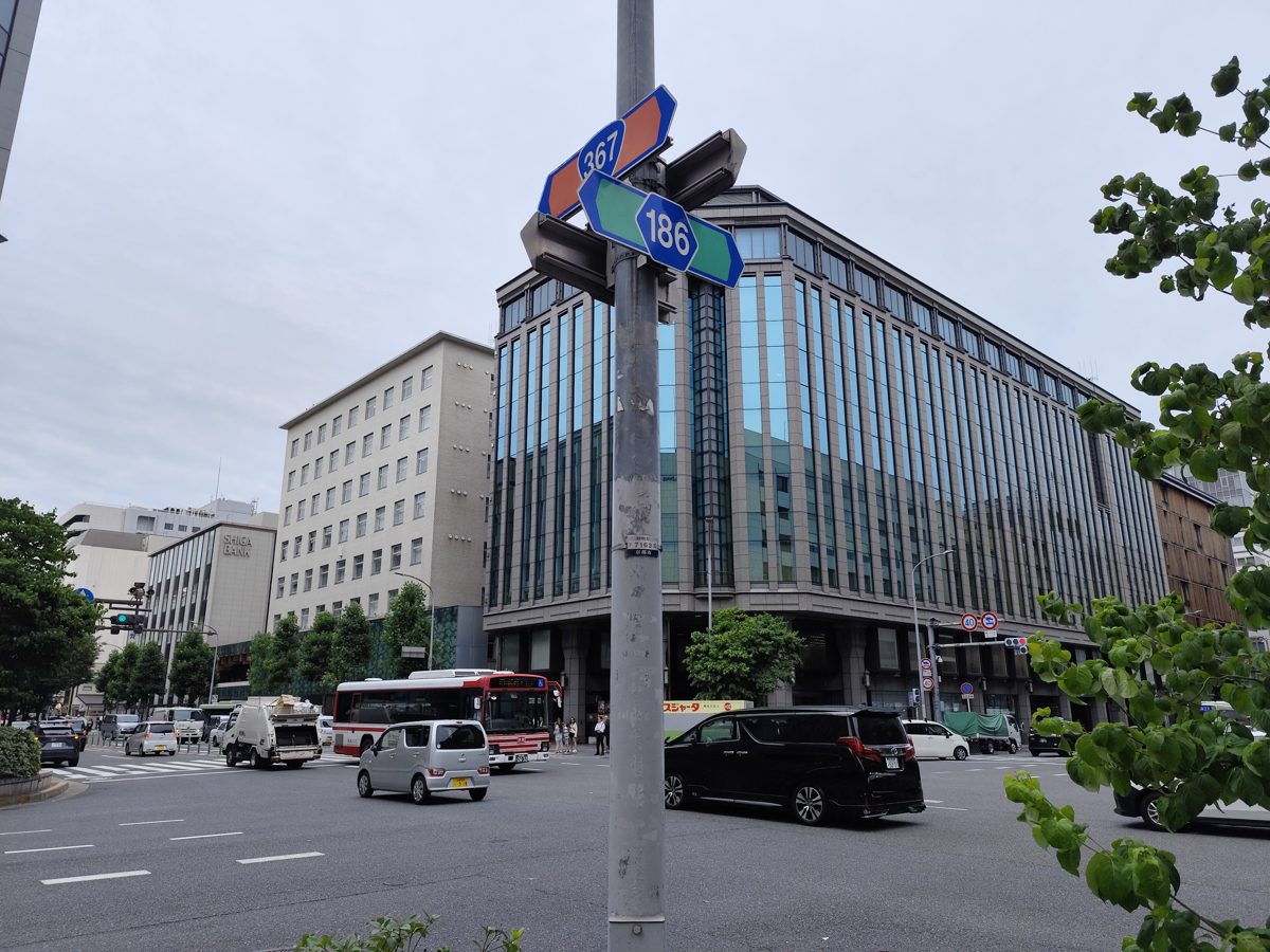 A wide street crossing with a city bus, cars and office buildings under a cloudy sky