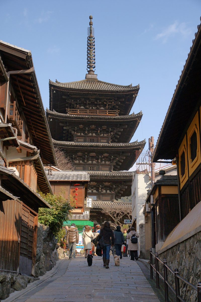A five-story wooden pagoda rising above a sloping stone lane with people walking