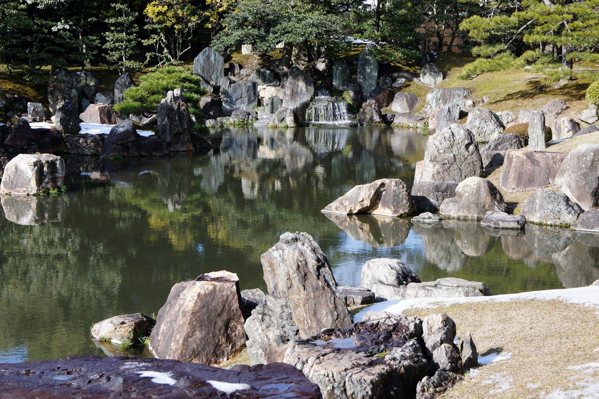 A pond with large rocks, pine trees and a lawn in a Japanese garden