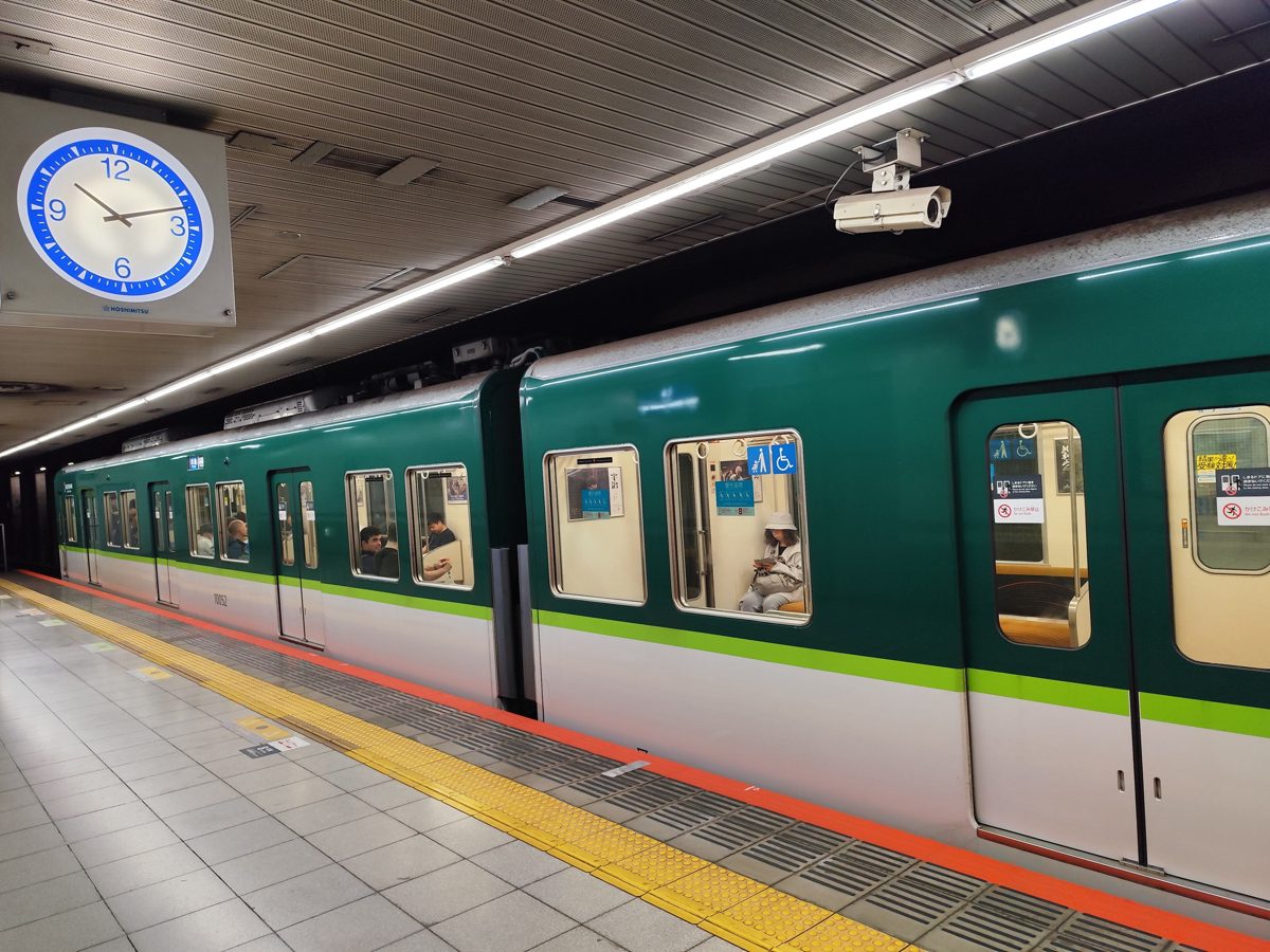 A green and white Keihan train stopped at an underground station platform