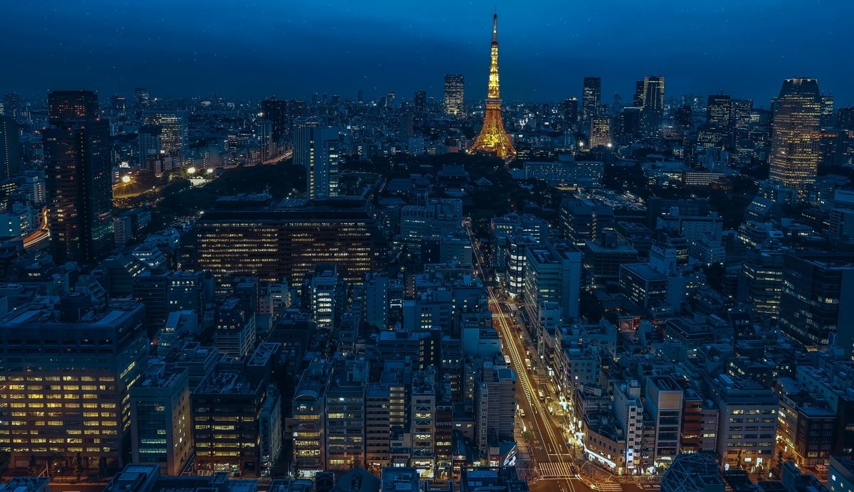 Lit office buildings and streets in Minato City at night, with Tokyo Tower in the distance