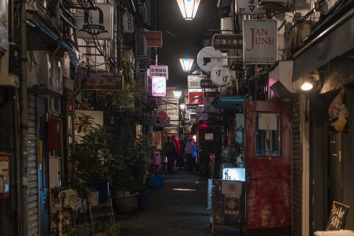 A narrow alley of small bars lit by lanterns and signs at night