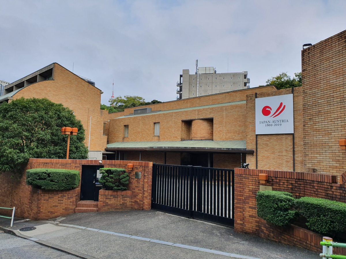 A brick embassy building and closed gate behind a hedge in Tokyo