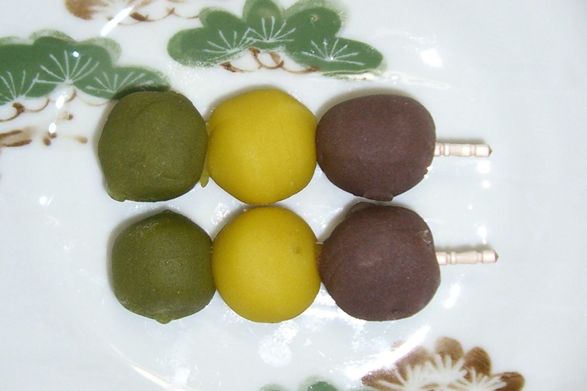 Two skewers of green, yellow and brown dumplings on a white plate