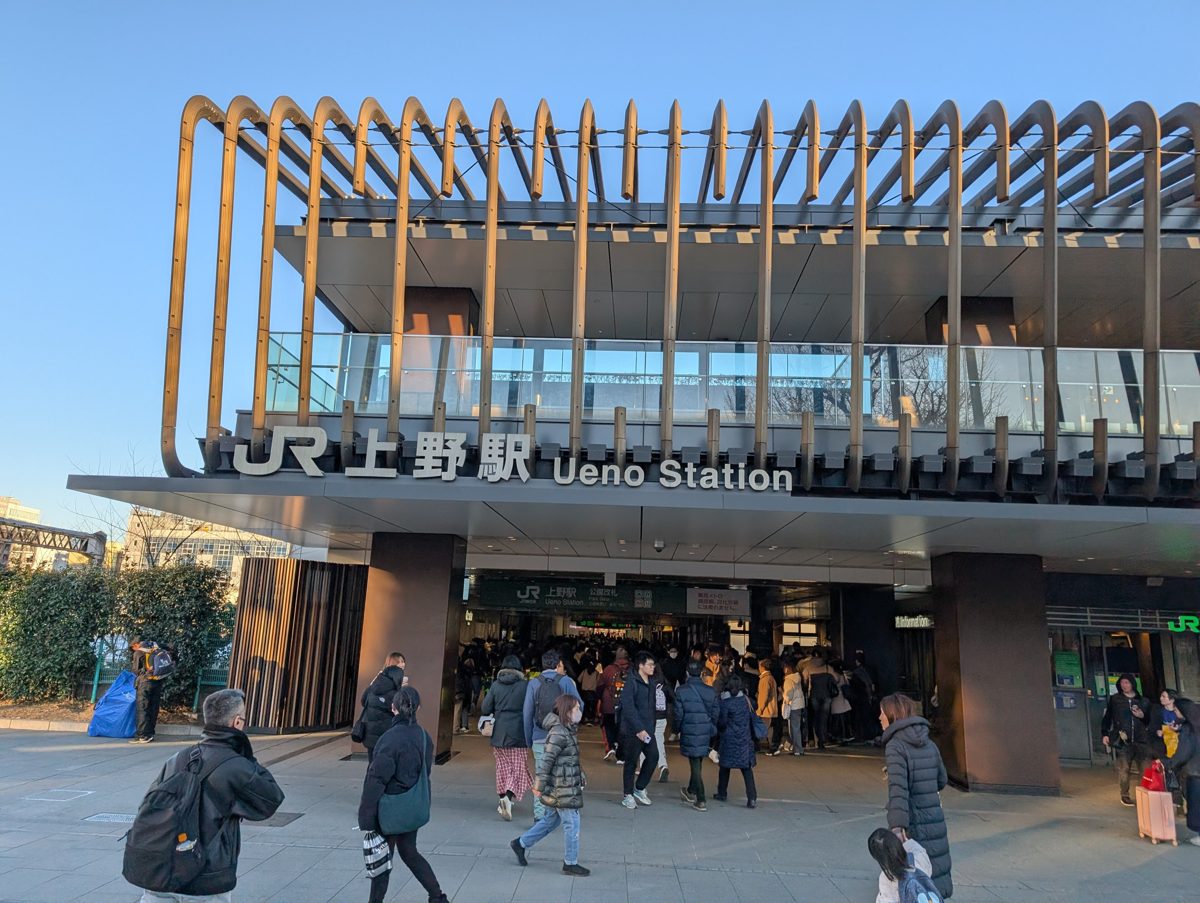 The entrance of a large railway station with a modern wooden canopy and people walking