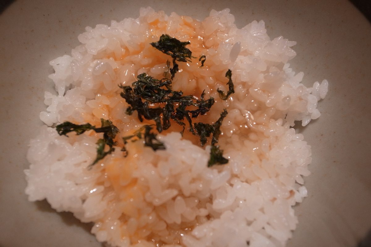 A bowl of white rice topped with raw egg and strips of seaweed