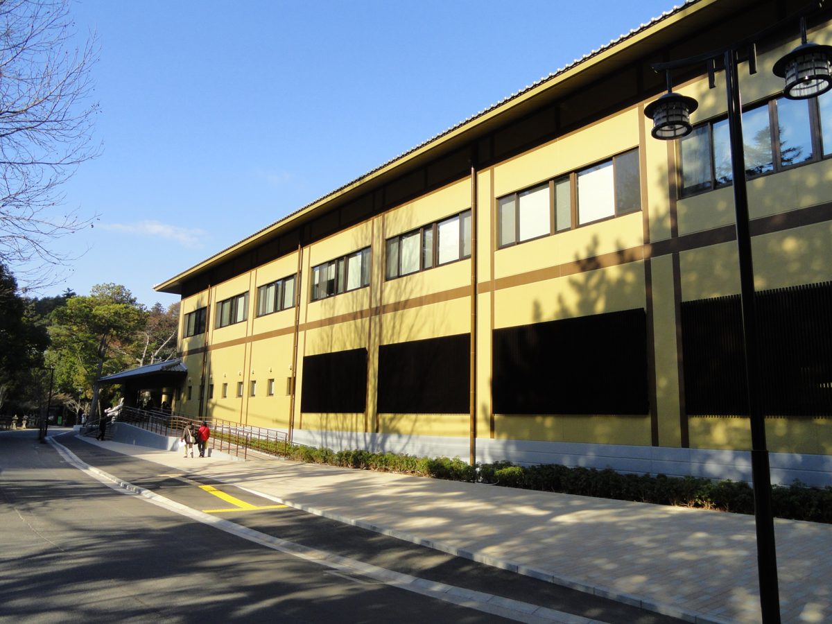 A long two-story yellow building with dark trim beside a quiet road on a sunny day