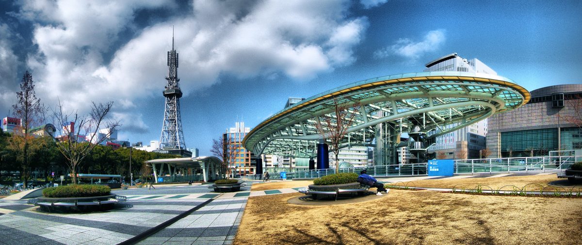 Oasis 21 glass roof structure with Nagoya TV Tower behind it under a cloudy blue sky