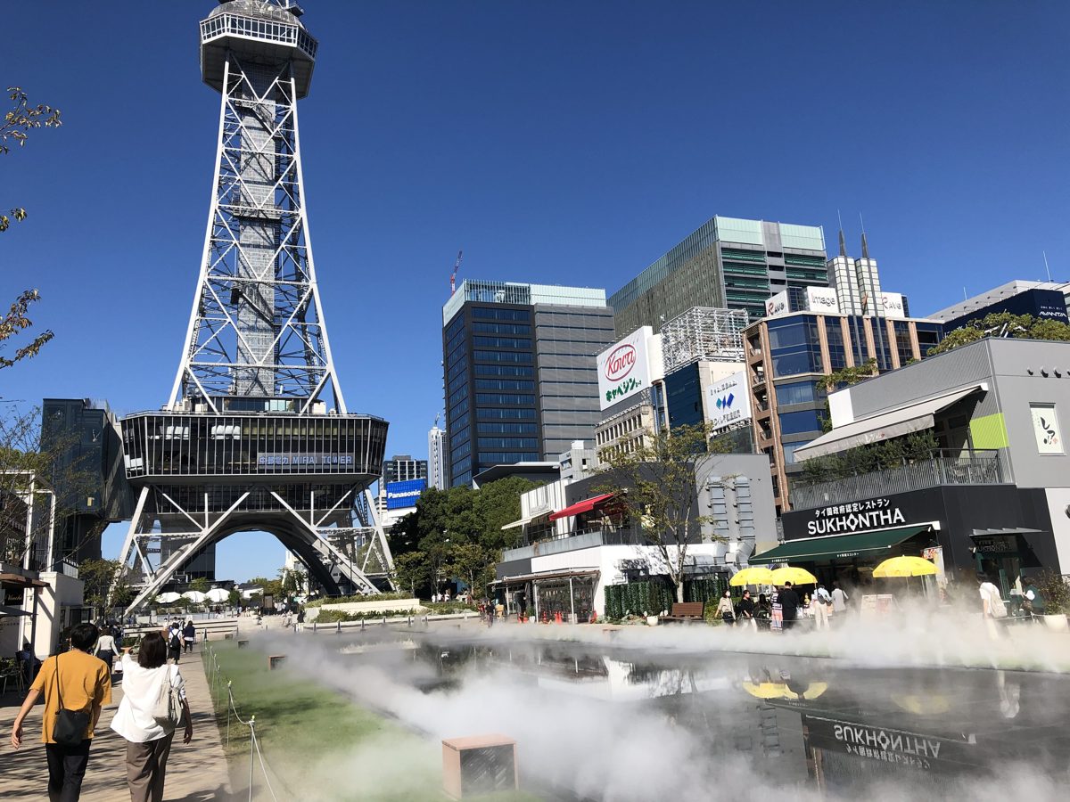 Mist rising from the ground in a plaza below Nagoya TV Tower, with people walking nearby