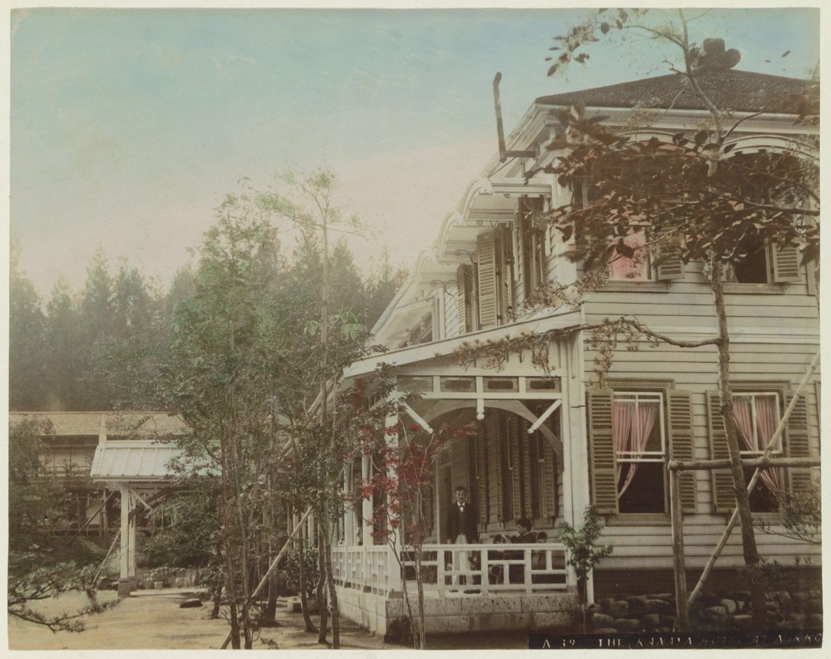A hand-colored old photograph of a two-storey Western-style wooden hotel building with a veranda among trees