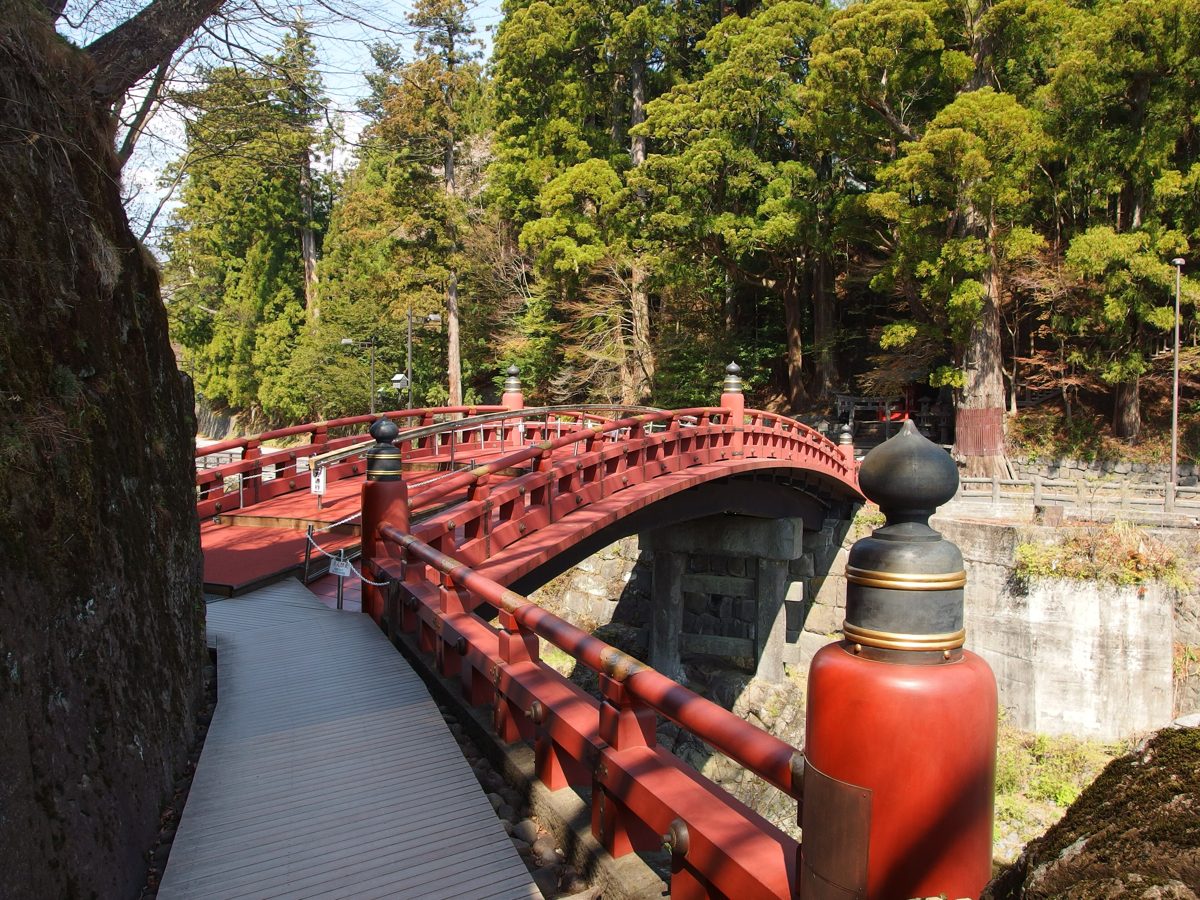 The red lacquered Shinkyo bridge over a river in Nikko, with spring trees