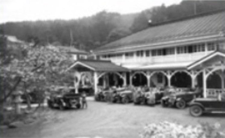 A black-and-white photograph of the Kanaya Hotel entrance with old cars parked in front
