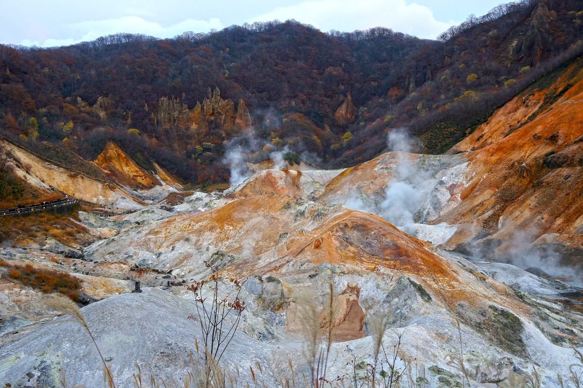 Steaming orange and gray volcanic ground in a valley of autumn trees at Jigokudani, Noboribetsu Onsen