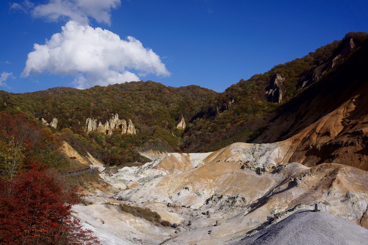 Jigokudani volcanic valley in Noboribetsu under a blue sky, with white and orange ground and autumn trees