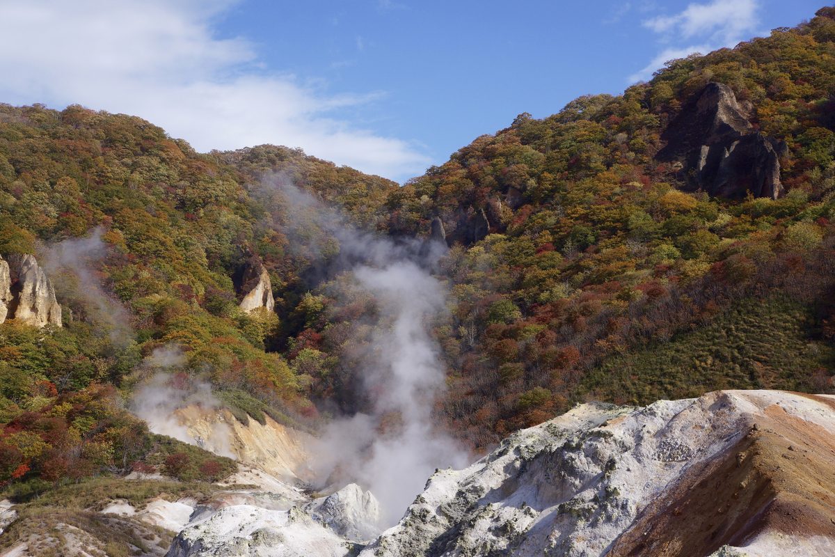 Steam rising from Jigokudani in Noboribetsu between wooded autumn hills