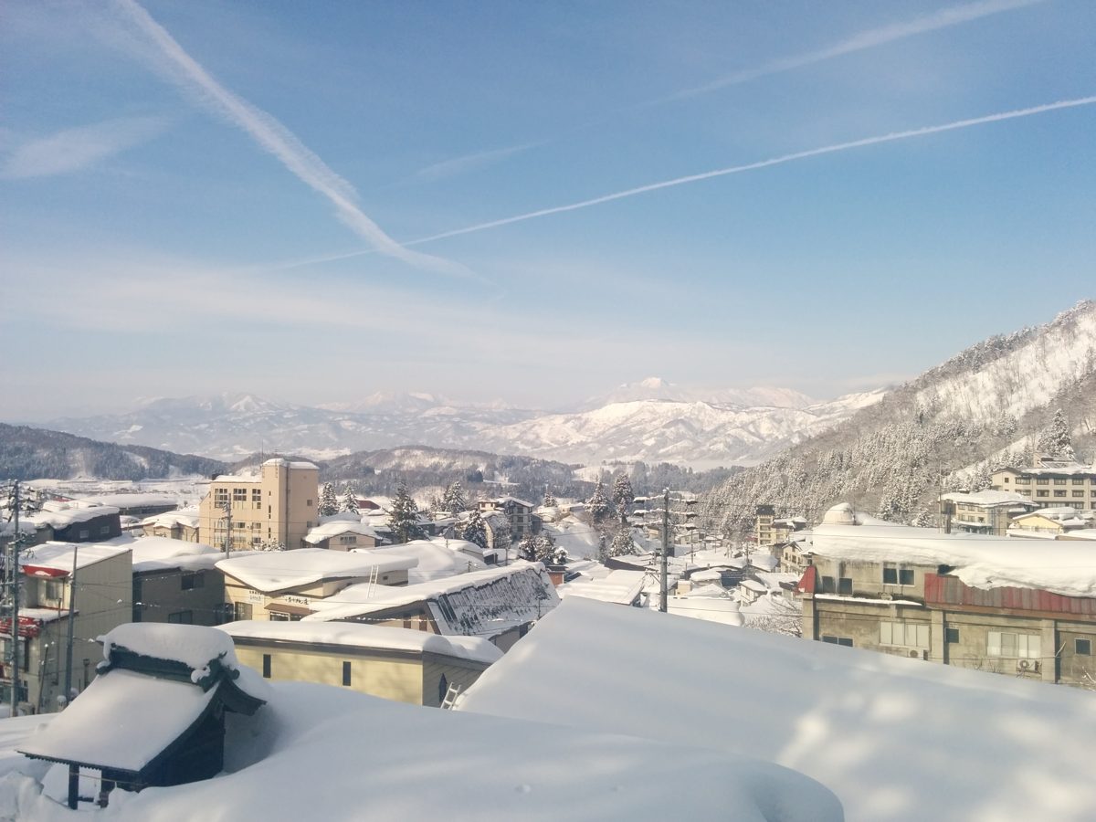 Snow-covered rooftops of a village with snowy mountains under a blue sky