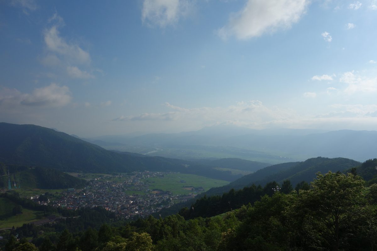 View from a hillside over a green valley and a town below, with mountains in the distance