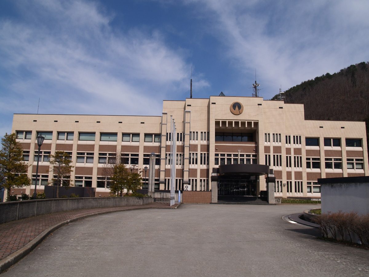 A beige municipal building under a blue sky with a curved driveway in front