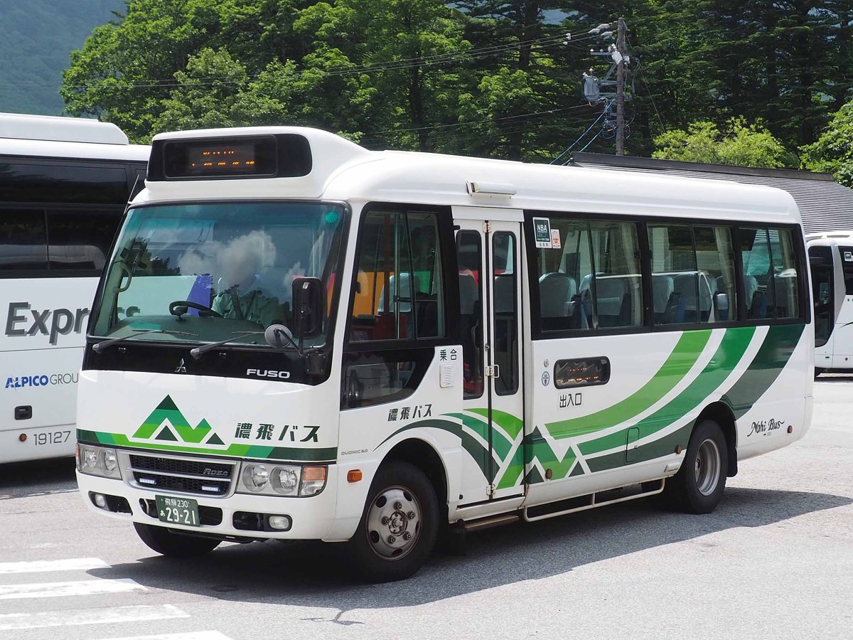 A white and green Nohi Bus minibus parked in a lot with trees behind