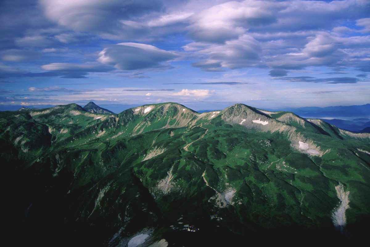 Green mountain ridges of the Northern Alps under a blue sky with clouds