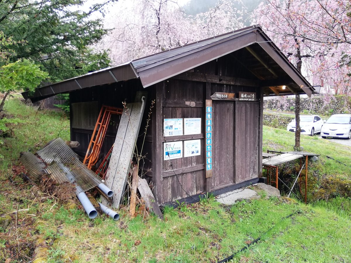 Small wooden hut beside a stream with cherry blossoms in spring