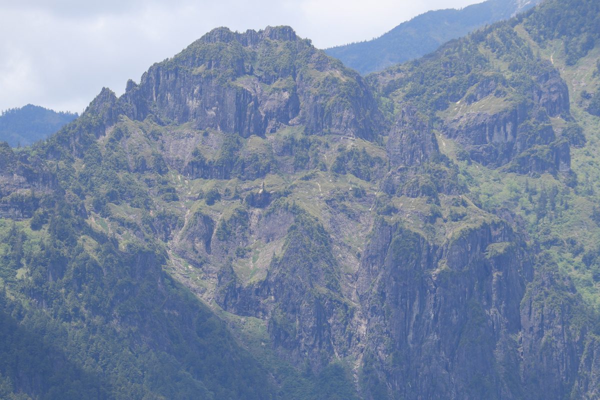 Rocky green slopes of Mount Shakujo under a blue sky, seen from Mount Yake