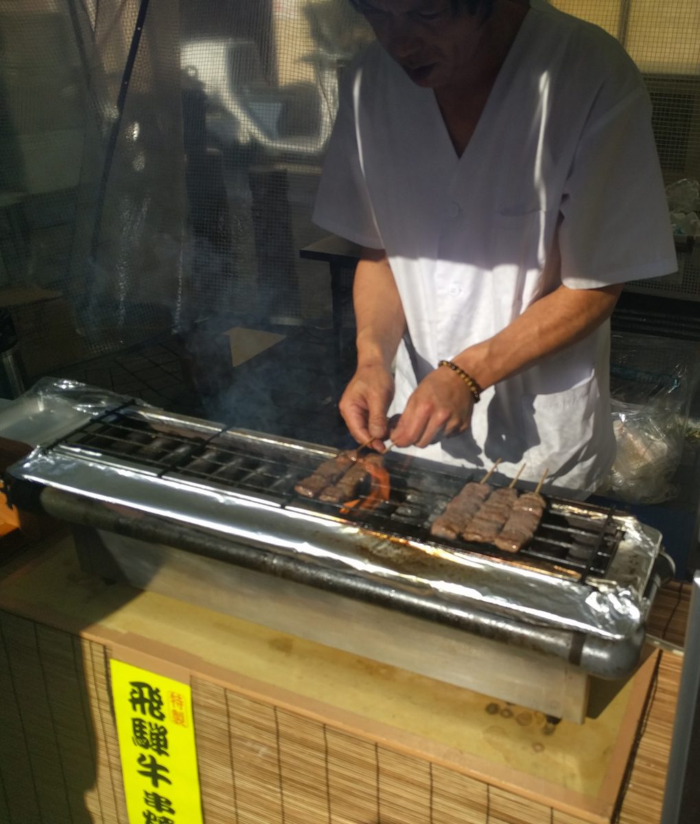Skewers of Hida beef cooking on a grill at a street stall