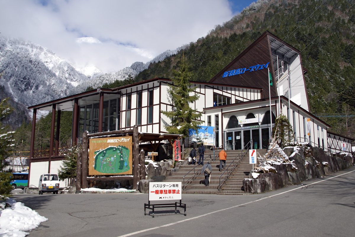 A timber-framed ropeway station building with steps and snowy peaks behind it