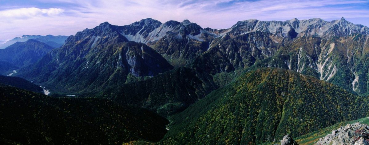 A wide view of a rocky mountain range above forested valleys