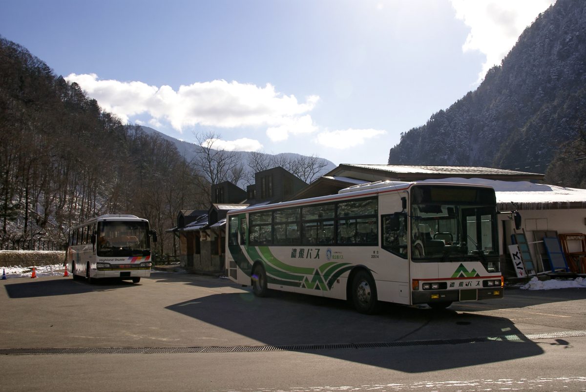 Buses parked at a bus stop in Shinhotaka Onsen, with mountains behind and a little snow on the ground