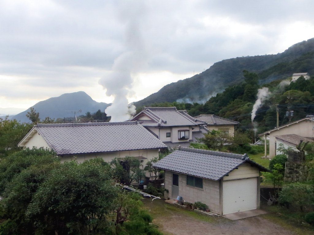 Columns of white steam rising from a hillside above tiled-roof houses