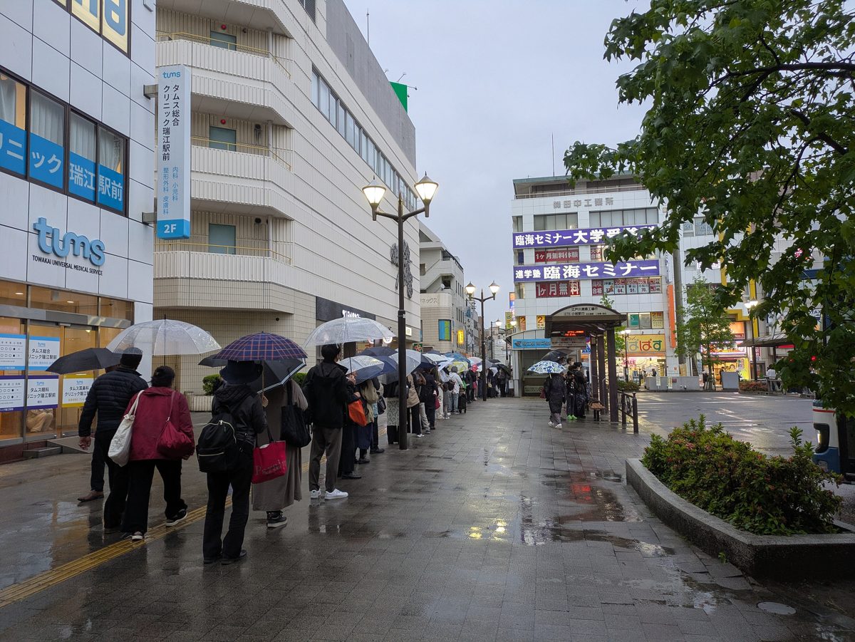 People with umbrellas walking and waiting for buses on a wet street outside a station in Tokyo