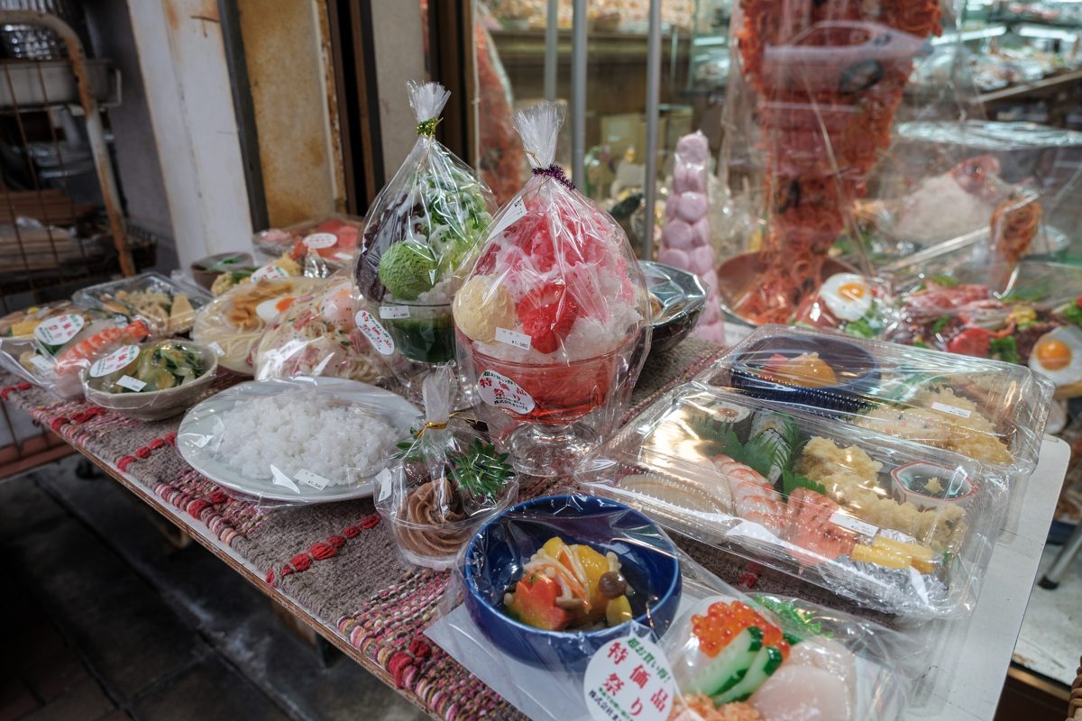 Plastic food samples of sushi, noodles and drinks on a store display table